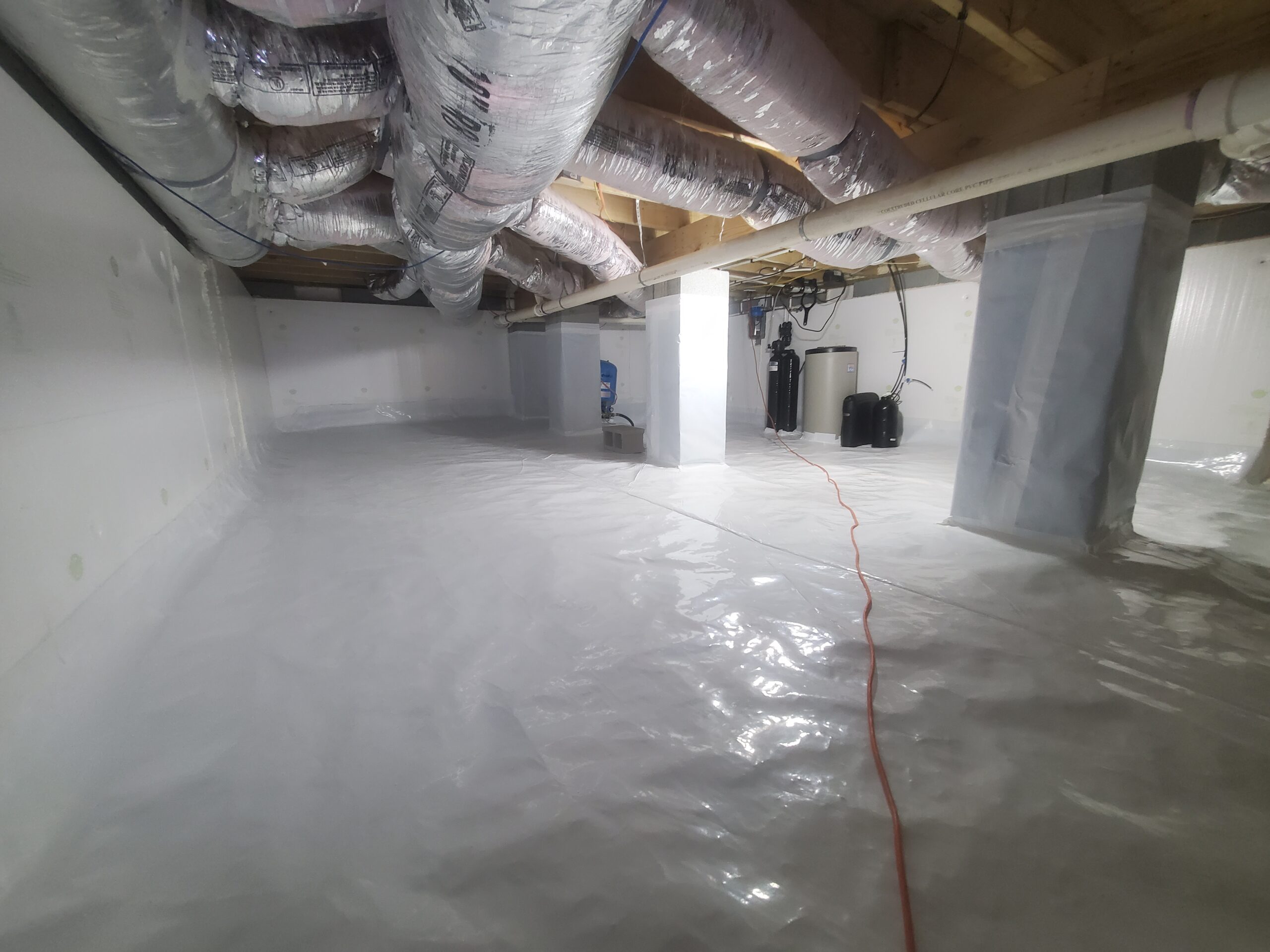A clean, encapsulated crawl space with white plastic sheeting on the floor and walls, visible ducts, support columns, and water treatment equipment in the background.