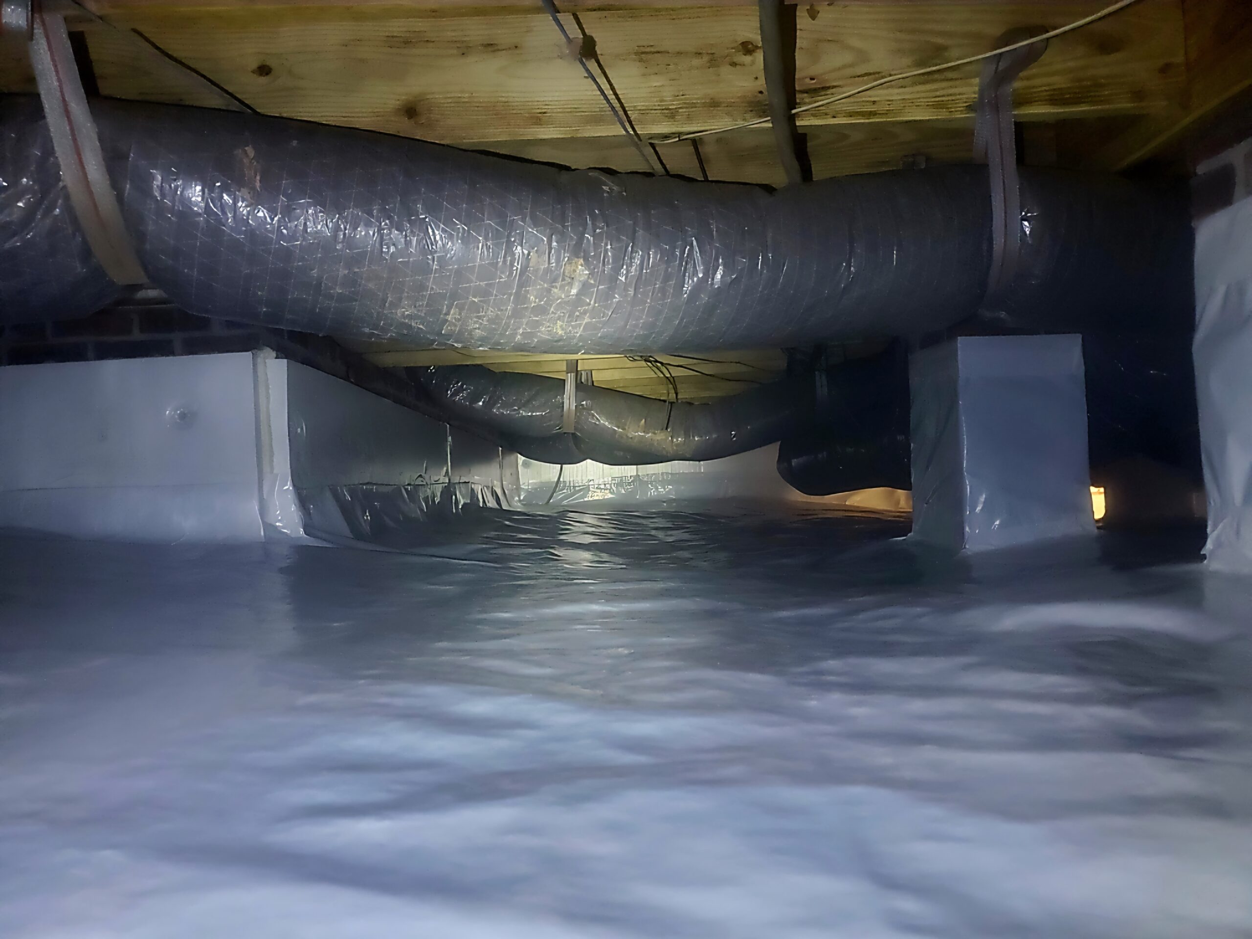Plastic-lined crawl space with insulated HVAC ductwork running along the ceiling and foundation walls.
