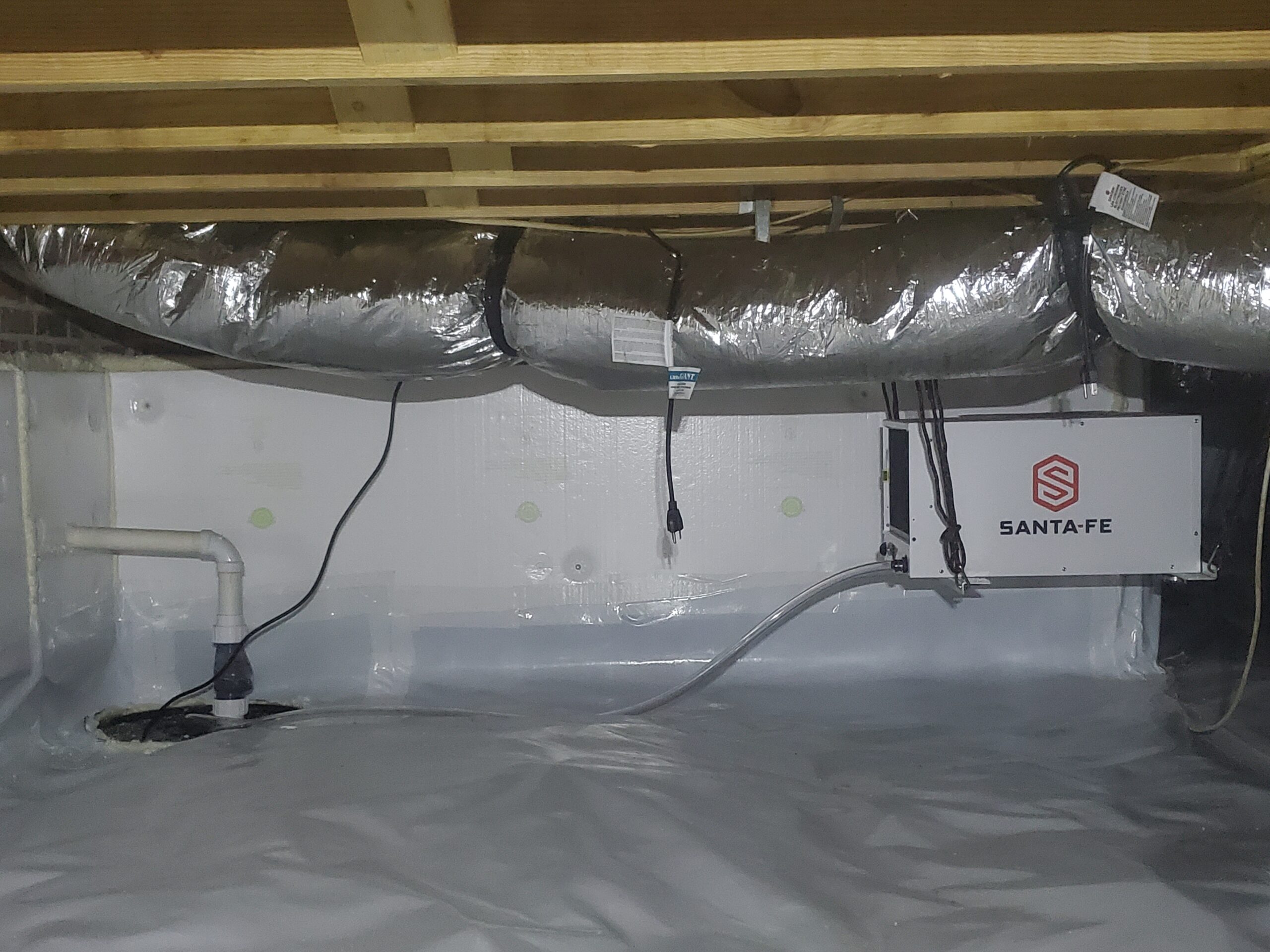 A crawl space with a plastic vapor barrier, insulated ductwork, a sump pump, and a Santa Fe dehumidifier installed on the wall.