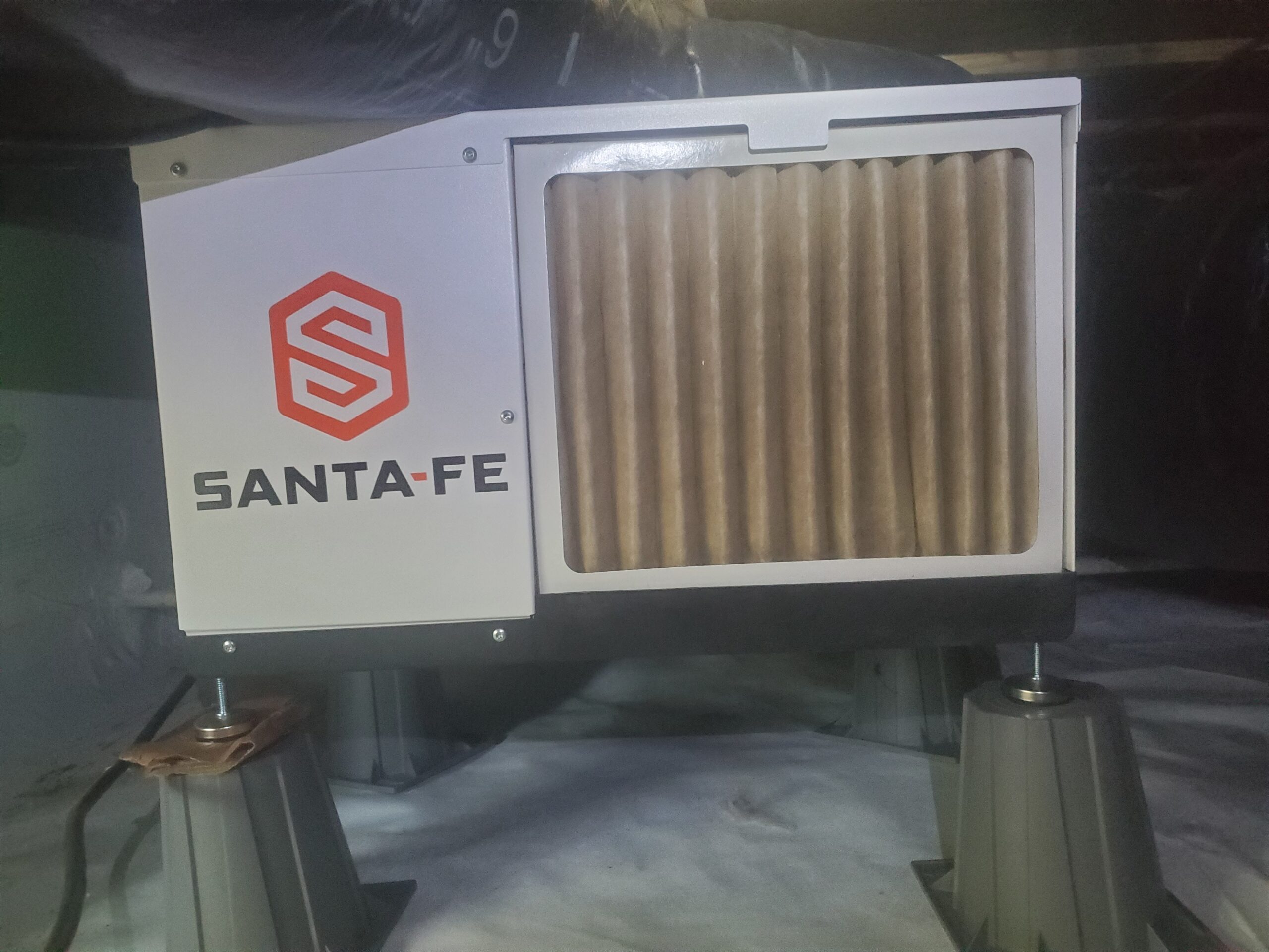 A Santa-Fe dehumidifier is elevated on plastic stands in a crawl space, with a visible pleated air filter in the front panel.