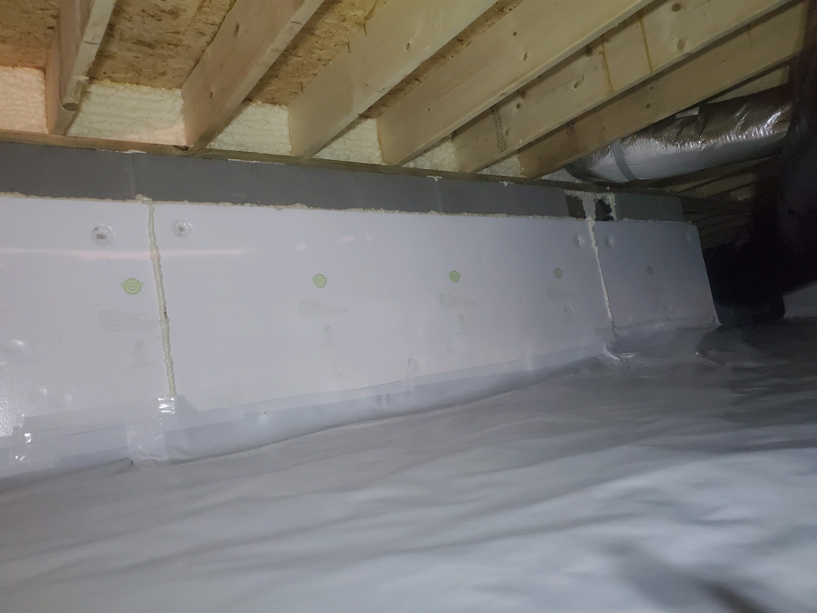 A crawl space with a plastic vapor barrier on the floor, foam board insulation on the walls, and exposed wooden floor joists above—ideal features for effective mold removal and prevention.